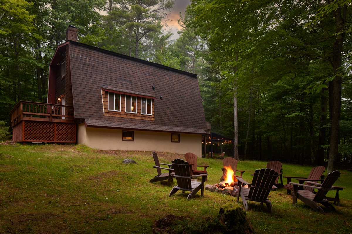 Fire pit circle staged with chairs arranged, view of the cabin exterior at dusk with the sky still holding color