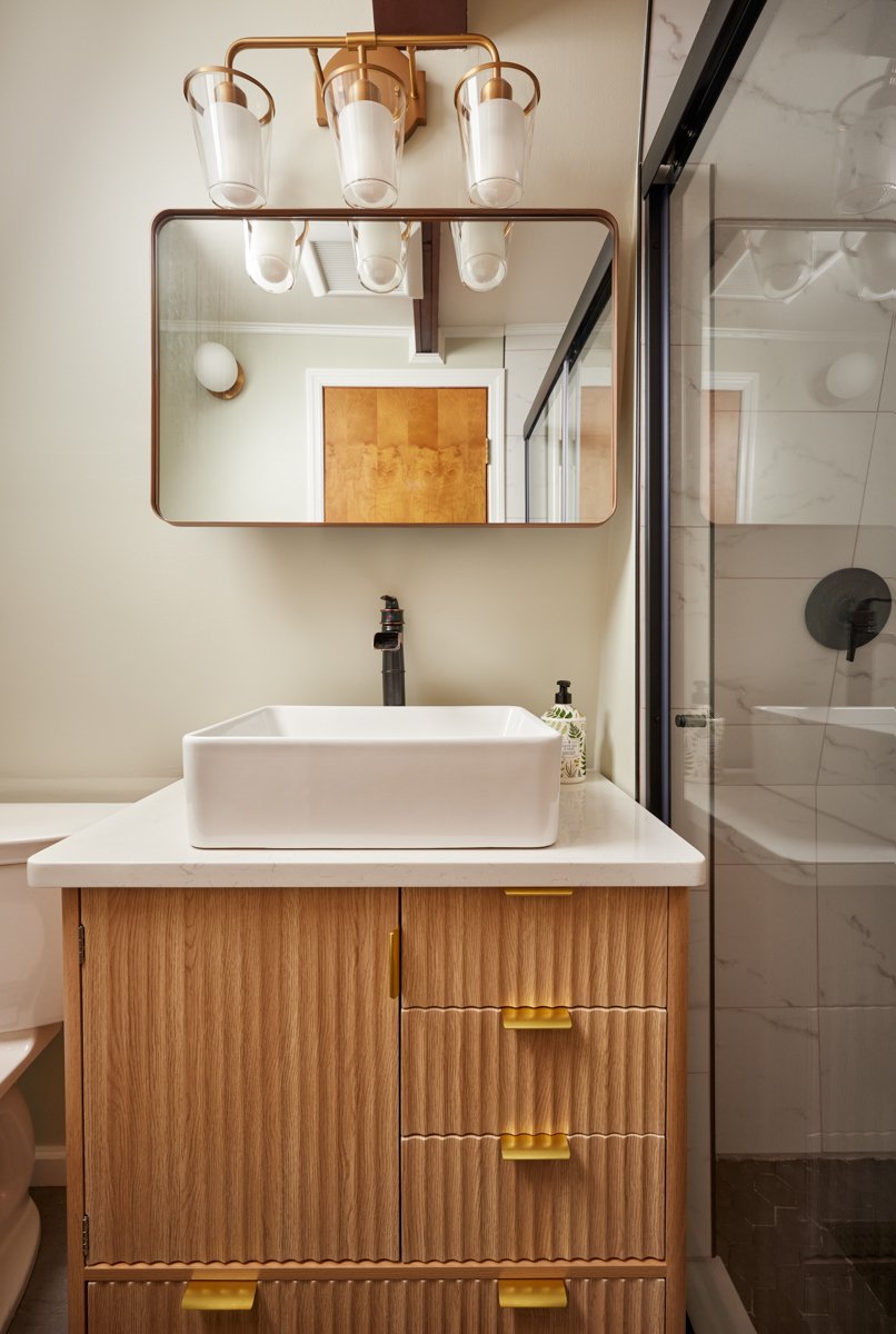 Finished Jay bathroom vanity with reeded wood cabinet, brass fixtures, and glass shower door