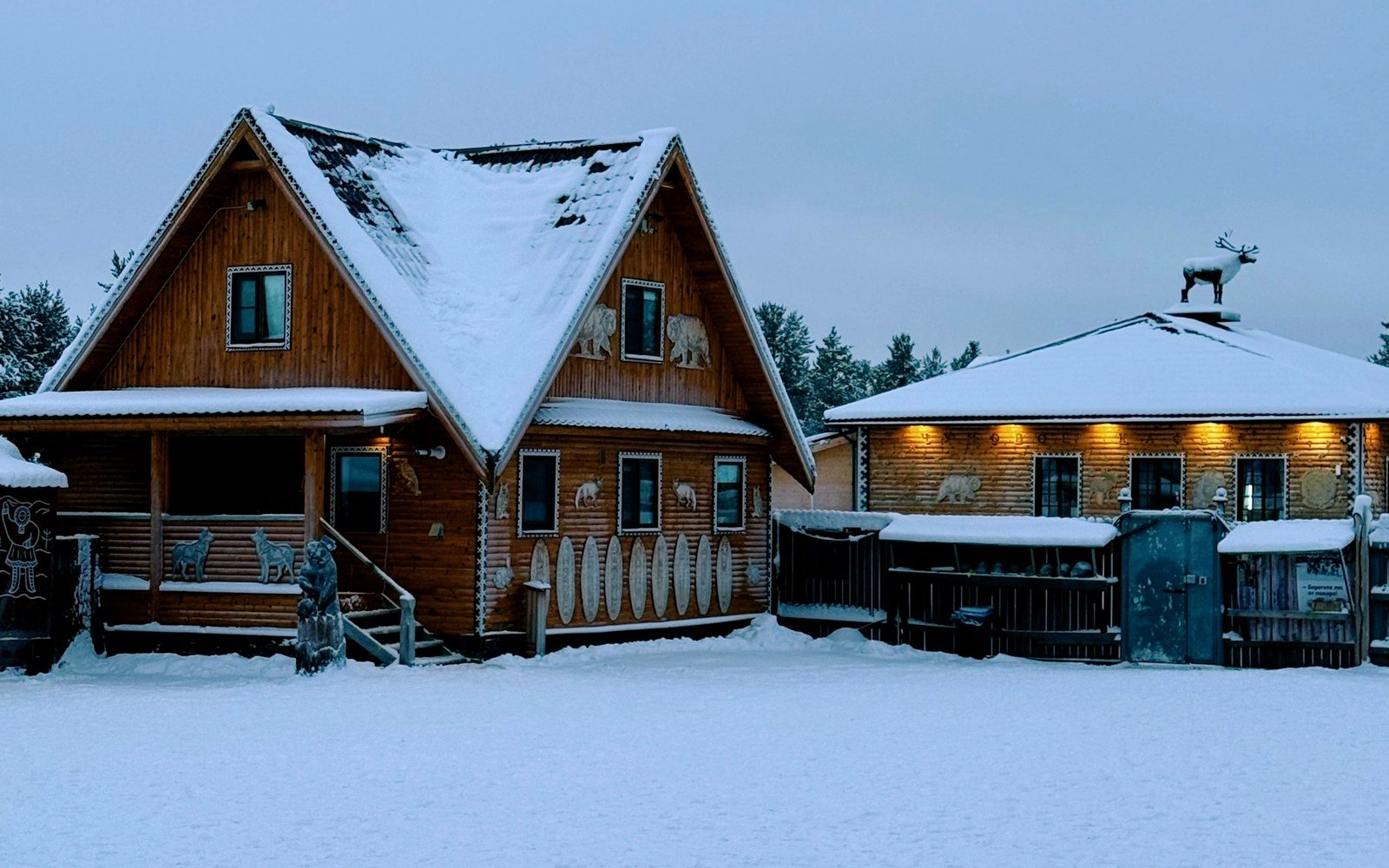 Snow-covered Adirondack cabin exterior with warm porch light at dusk